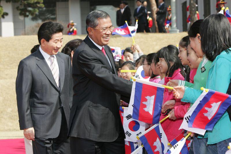 [캄보디아 총리 공식환영식에서 양국 국기를 흔드는 어린이들의 환영을 받는 양국 정상]